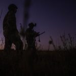 Two soldiers walk through a field at dusk.