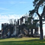 Casa destruída com restos carbonizados e uma árvore