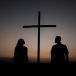 Silhueta de casal ao lado de uma cruz ao pôr do sol — fé em zonas de conflito