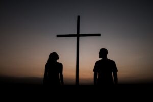 Silhueta de casal ao lado de uma cruz ao pôr do sol — fé em zonas de conflito